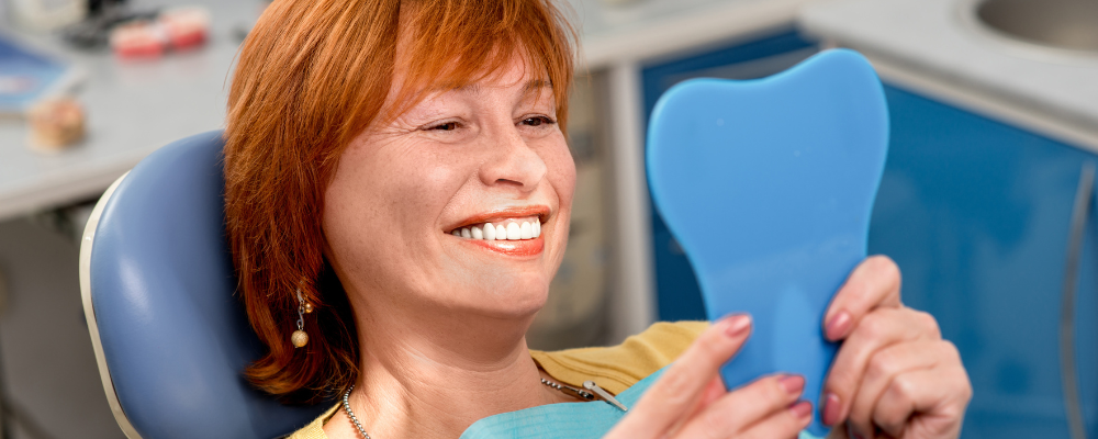 Woman smiling into mirror after having new dentures