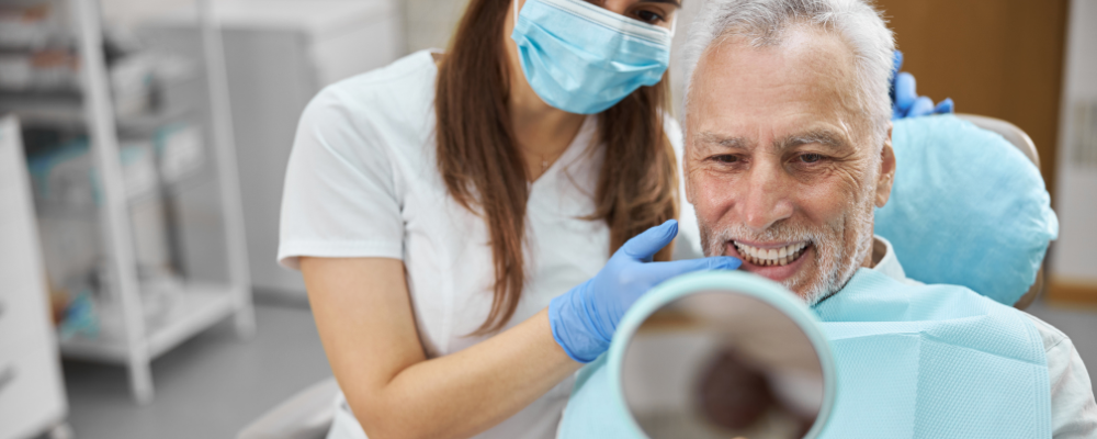man smiling into mirror as female dentist points towards his new full smile