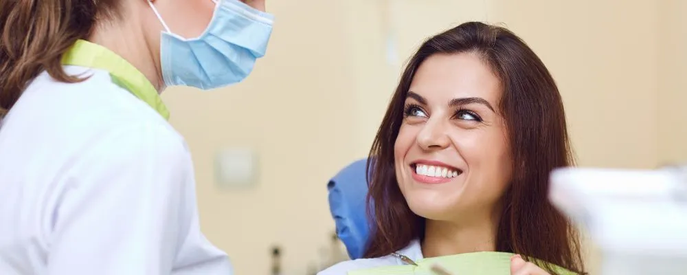 woman listening to female dentist in dental chair with white straight teeth